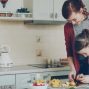 Young pretty mother teaching her cute daughter to cut vegetables properly. Little smiling girl cooking together with loving mom at home in modern kithcen