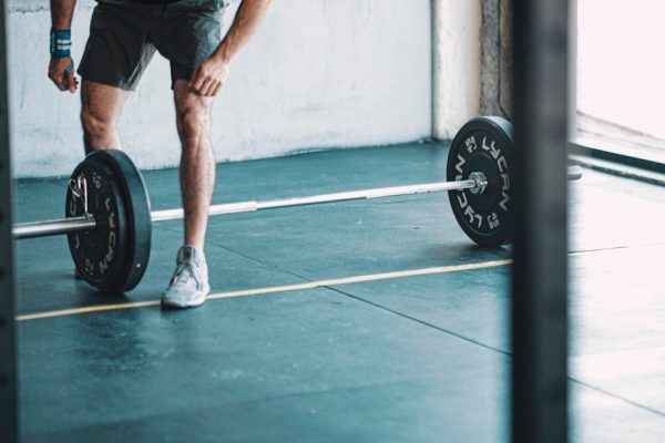 man in black t-shirt and black shorts holding black barbell